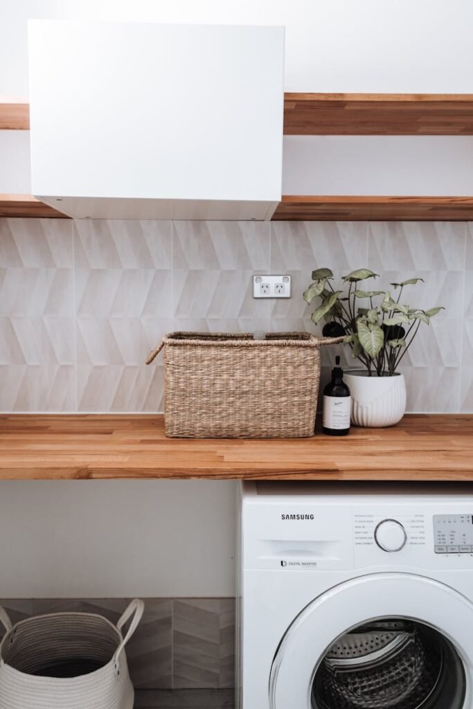 Bright and tidy laundry room featuring a washing machine, wicker basket, and potted plant on a wooden counter.