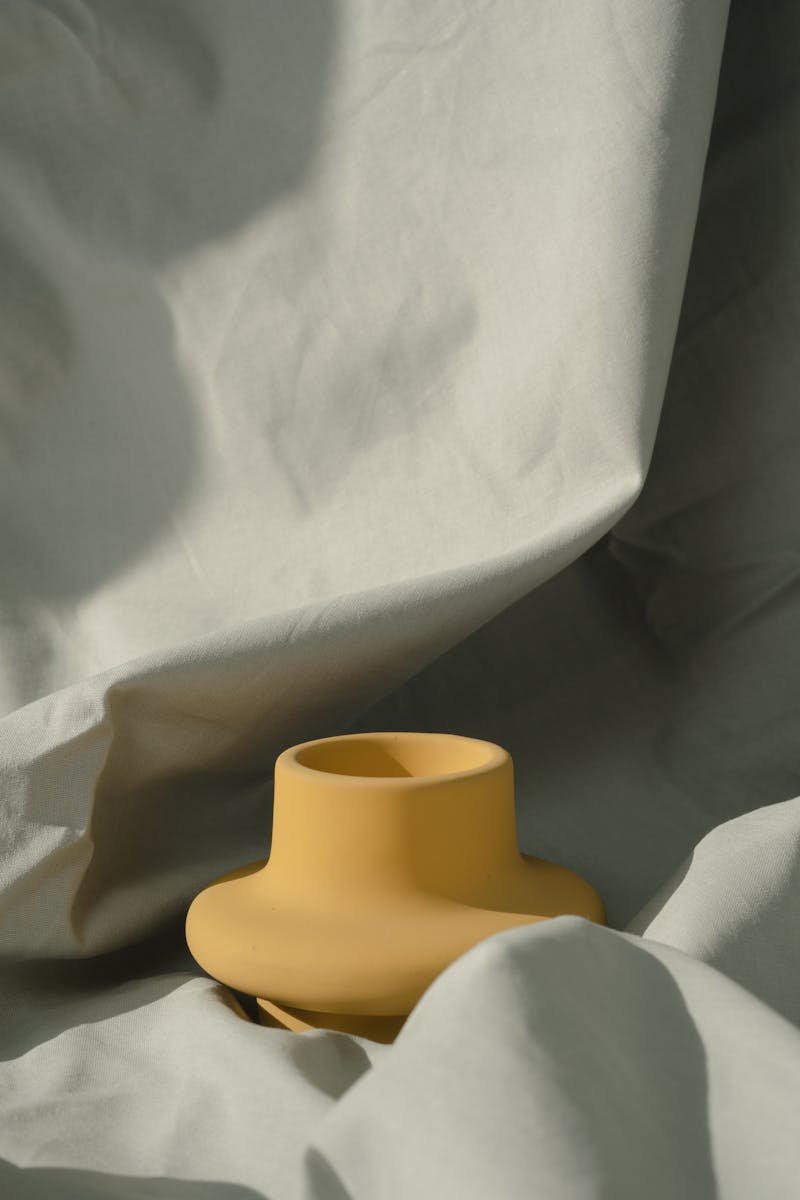 Artistic capture of a yellow vase on draped cloth under soft lighting, perfect for a minimalist style.