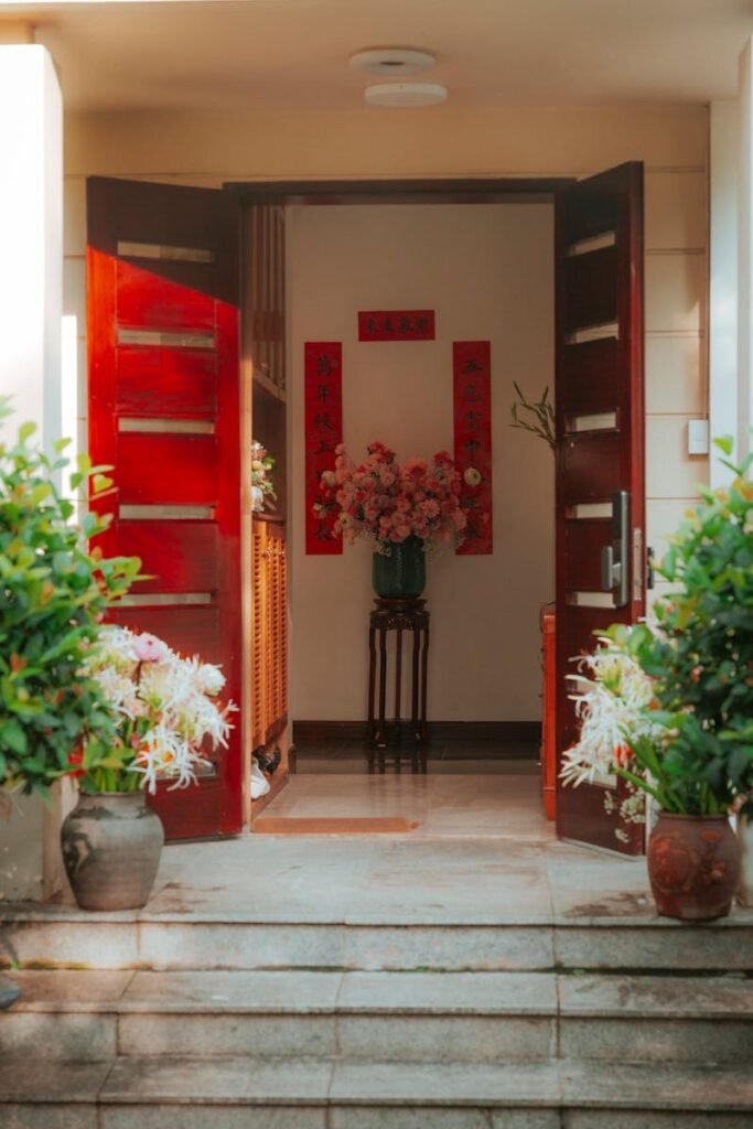 Stylish home entrance with red double doors, floral decor, and vibrant plants.