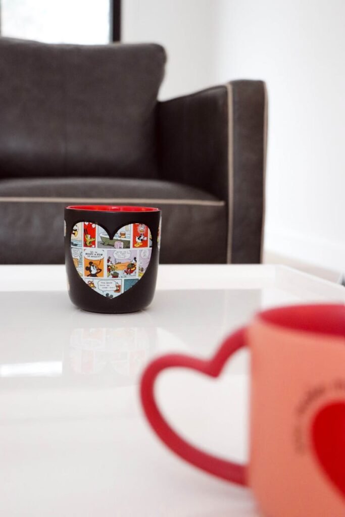 A heart-themed mug sits on a table in a contemporary living room with a couch.