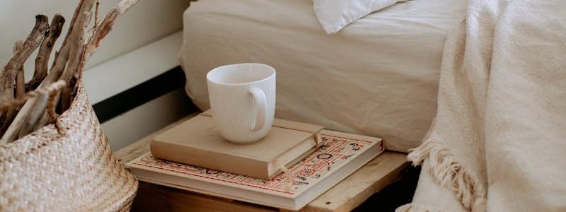 Comfortable cozy bedroom with bed wooden shelves with book and cup while wicker basket with sticks placed on ethnic styled rug