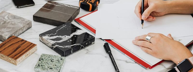 Architect works on design with material samples, sketching ideas on a marble table.
