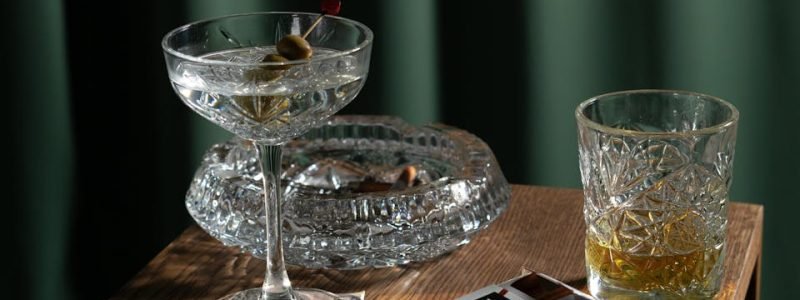 A classic cocktail and whiskey glass on a wooden table with cash and cigarettes.