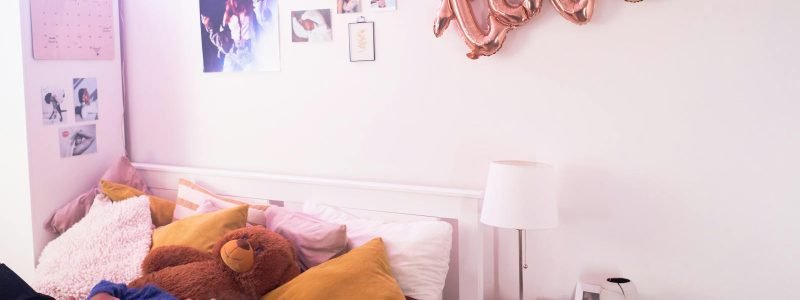 Teen girl relaxing in cozy bedroom with love balloon decor and teddy bear, capturing warm, peaceful vibes.